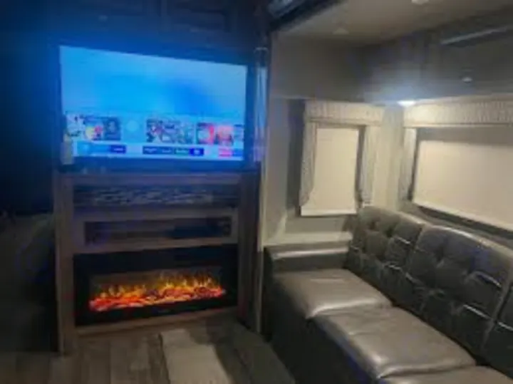 Cozy RV rental living area with a large TV, glowing electric fireplace, and dark sofa. Perfect for relaxing nights on the road.. Jayco Precept Prestige 2021