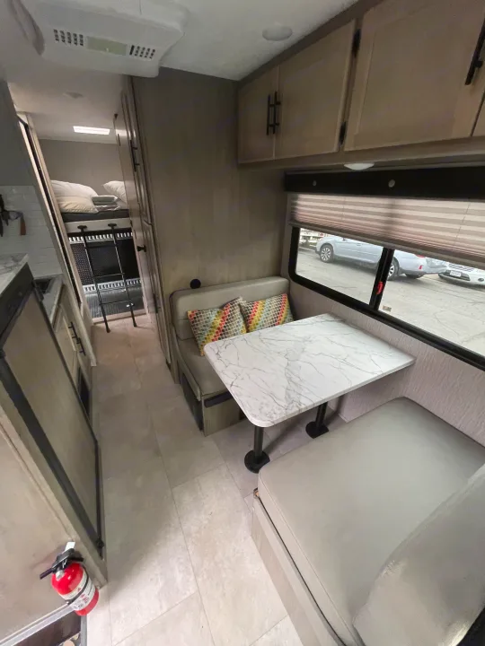 This RV rental interior features a dinette with a marble-look table, overhead storage, and a glimpse of the bunk bed area.. Coachmen Crosstrail 20XG 2022