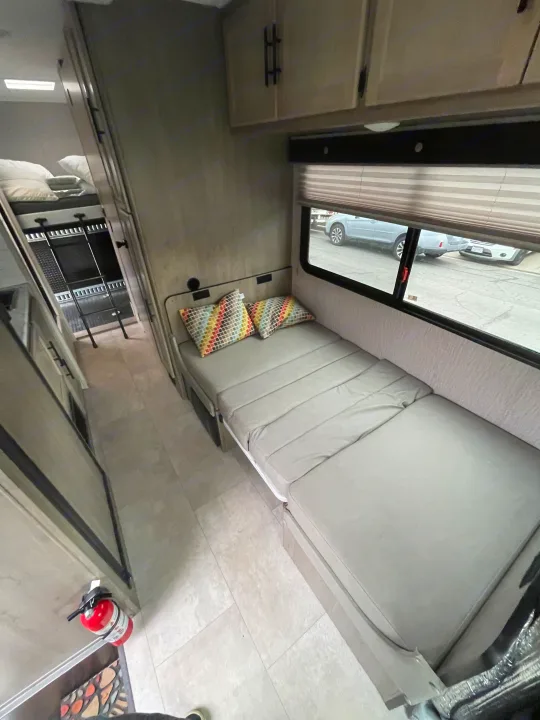 Inside this RV rental: a compact living space with a pull-out bed, patterned pillows, overhead storage, and bunk beds visible down the hall.. Coachmen Crosstrail 20XG 2022