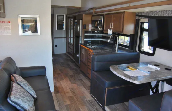 Explore a modern RV rental interior featuring a full kitchen, dining booth, and comfortable sofa, ideal for travel.. Thor Motor Coach Outlaw 2023