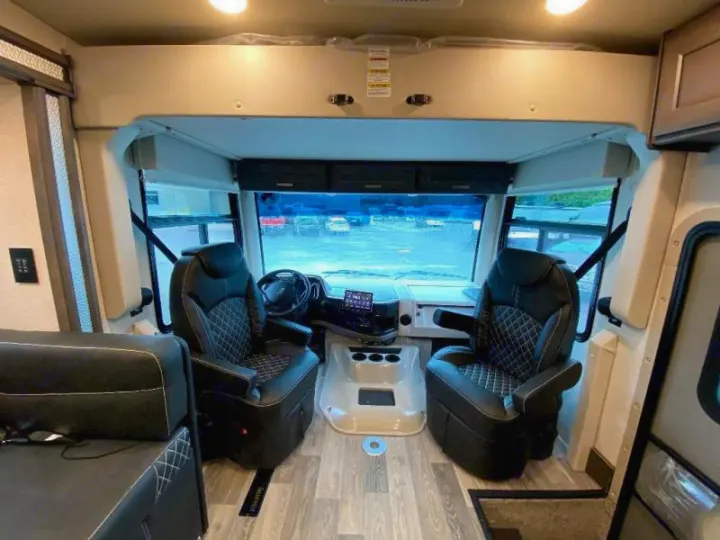 Detailed view of an RV rental's front cabin, showing the driver and passenger seats, dashboard, and windshield.. Thor Motor Coach Outlaw 2023
