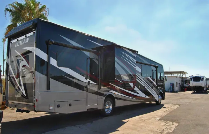 Sporty black "Outlaw" motorhome with bold graphics and extended slide-out, parked on a sunny lot, ideal for rv rental.. Thor Motor Coach Outlaw 2023
