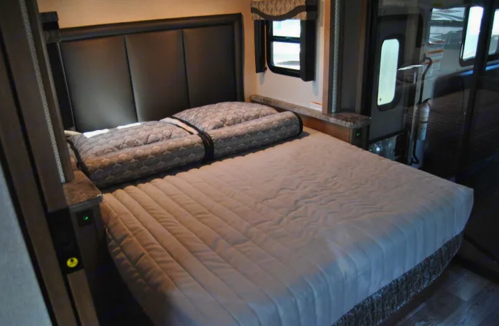 This RV rental bedroom features a comfortable bed, stylish headboard, and window, providing a cozy sleeping area.. Thor Motor Coach Outlaw 2023