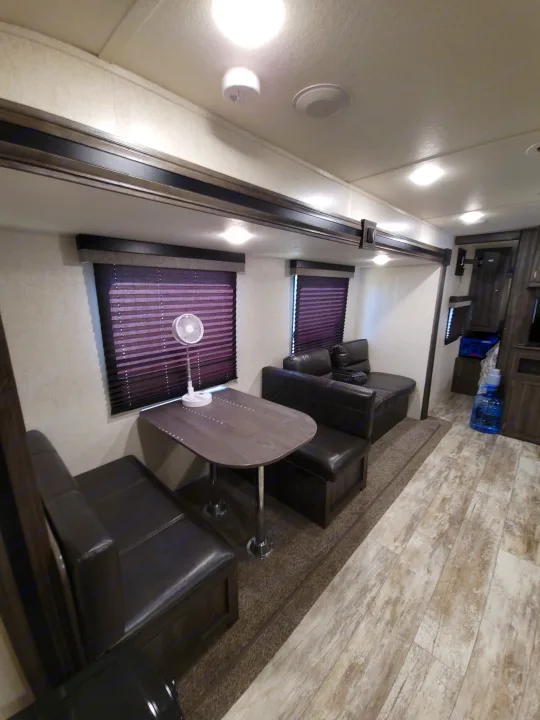Modern rv rental interior: dark dinette, comfy L-shaped seating, pleated blinds, and wood-look flooring create a cozy living space.. Highland Ridge RV Open Range Conventional OT26BHS 2019