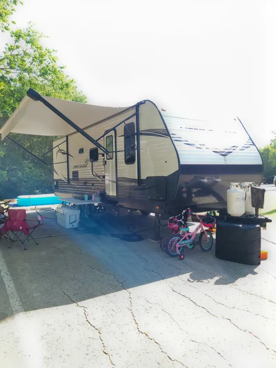 An RV rental set up at a bright campsite with an extended awning, chairs, a pool, and kids' bikes.. Highland Ridge RV Open Range Conventional OT26BHS 2019