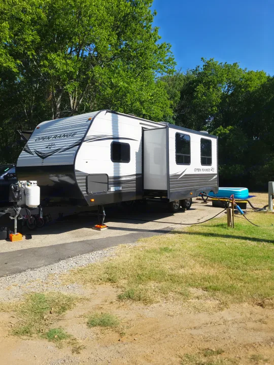 RV rental parked at a serene campsite with trees & blue sky. Features an extended slide-out and hookups.. Highland Ridge RV Open Range Conventional OT26BHS 2019