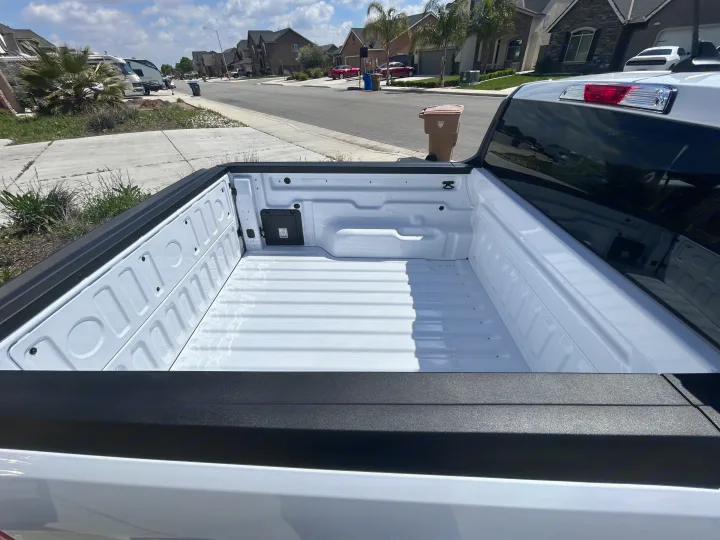 Inside a clean, white truck bed looking out at a suburban street with parked RVs. Ready for an rv rental adventure or gear transport.. Ford Maverick 2024