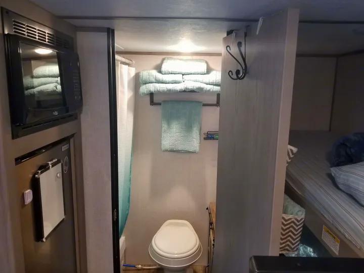 Compact RV rental interior featuring a kitchenette, bathroom with shower/toilet, and cozy bunk bed area, showcasing efficient use of space.. Coleman Lantern 17B 2023