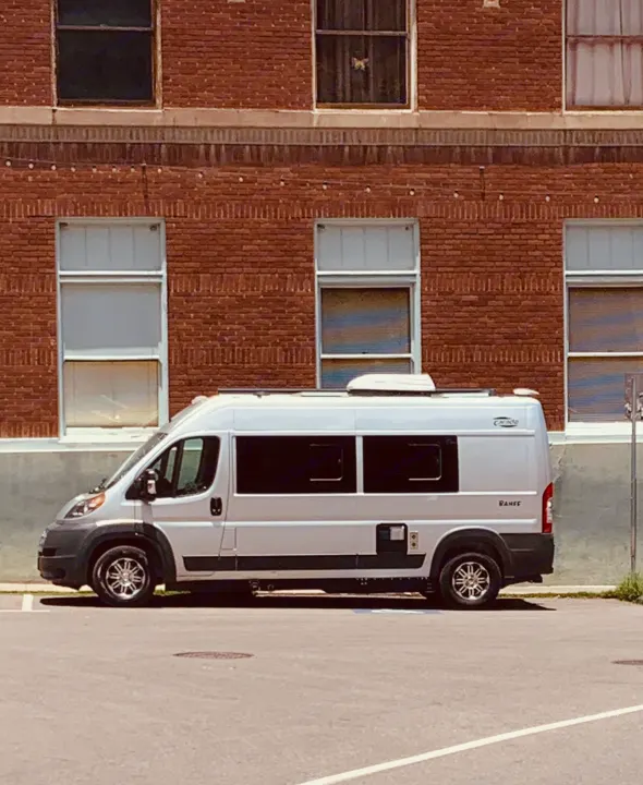 A white rv rental camper van is parked by a brick building, its compact size ready for travel adventures.. Carado Carado Class B 2018
