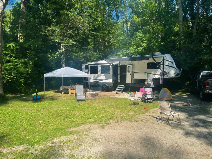 An RV rental provides a relaxing campout experience at this shaded forest campsite, featuring a canopy, picnic area, and chairs.. Keystone RV Sprinter 2021