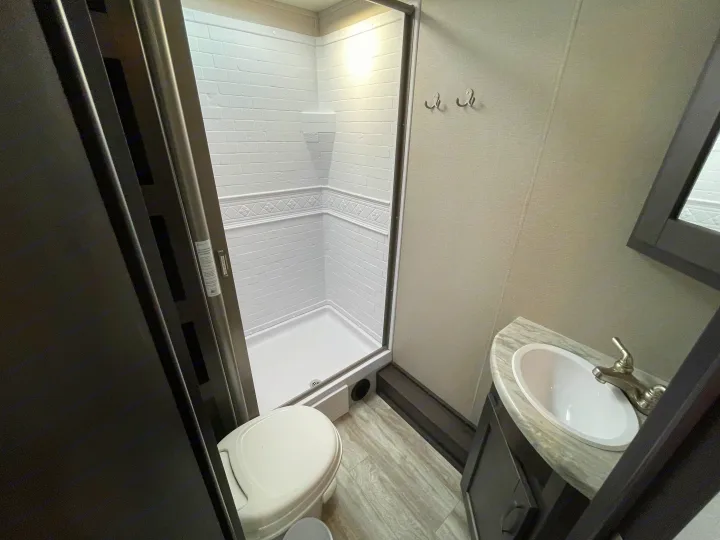 Bright, compact RV rental bathroom with a white shower, toilet, and vanity with a sink, perfect for on-the-go comfort.. Grand Design Transcend Xplor 2020