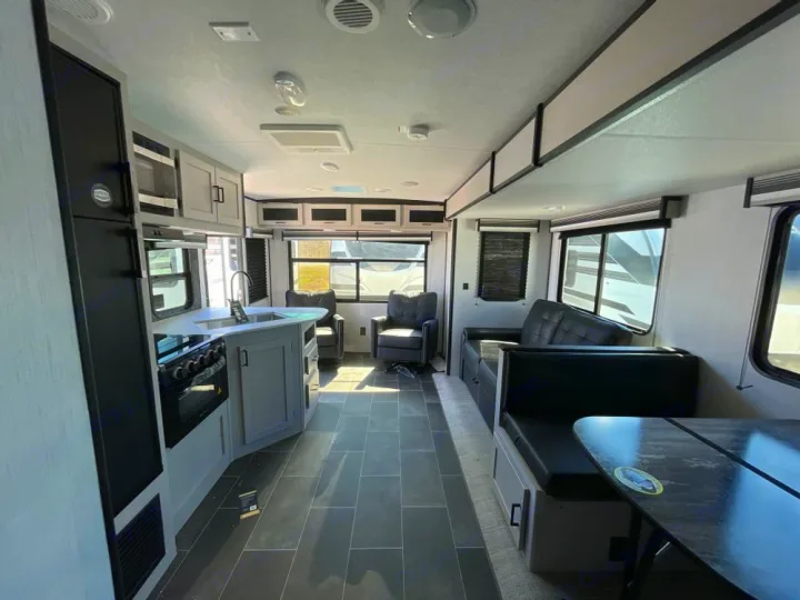 Bright RV rental interior with a modern kitchen, comfortable sofa, and dinette. Grey flooring and white cabinets.. Heartland RVs Mallard 2022