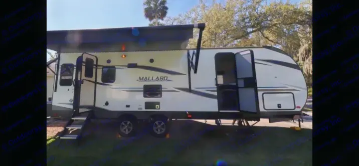 This white Mallard travel trailer RV rental, with an extended awning & open door, is ready for adventure at a sunny campsite.. Heartland RVs Mallard 2022