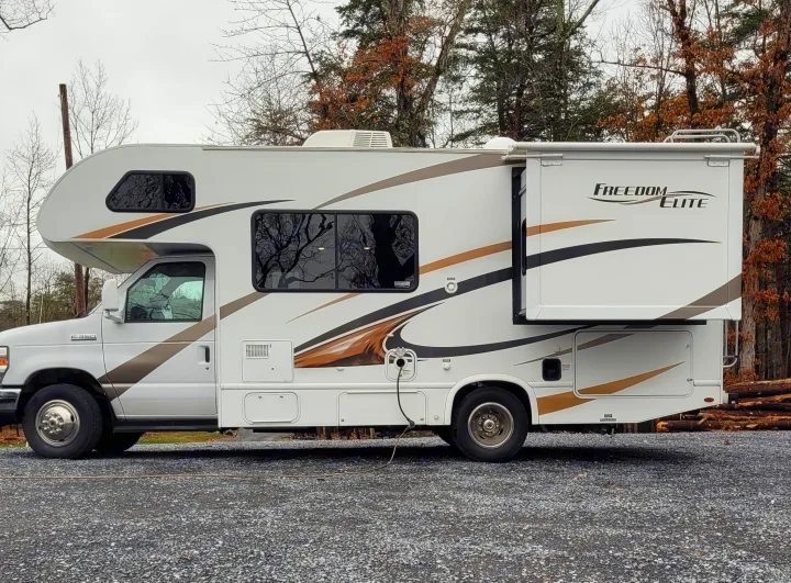 White Class C RV rental with extended slide-out parked on gravel, amidst trees, ready for your next adventure.. Thor Freedom Elite 2017