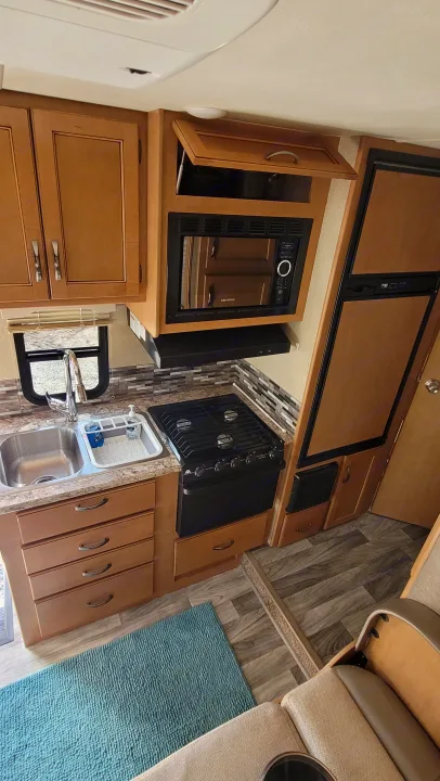 Spacious RV rental kitchen area features a stovetop, microwave, double sink, wood cabinets, and vinyl flooring.. Thor Freedom Elite 2017