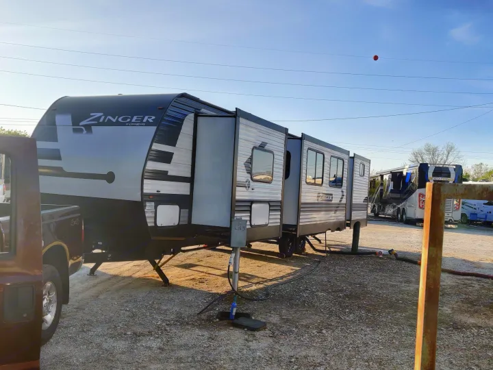 Zinger travel trailer, likely an rv rental, with slide-outs extended in a gravel RV park. Visible hookups and another RV.. Crossroads RV Zinger 2022