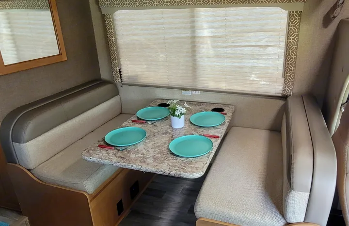 Inside an RV rental, a cozy dinette area is set with turquoise plates on a patterned table, ready for dining.. Thor Freedom Elite 2017