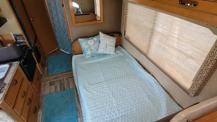 Inside a cozy RV rental: beach-themed bed, compact kitchen with sink/stove, and light wood cabinetry.. Thor Freedom Elite 2017
