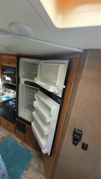 Inside an RV rental: an open refrigerator and freezer, with a kitchen area, stove, and dinette visible.. Thor Freedom Elite 2017