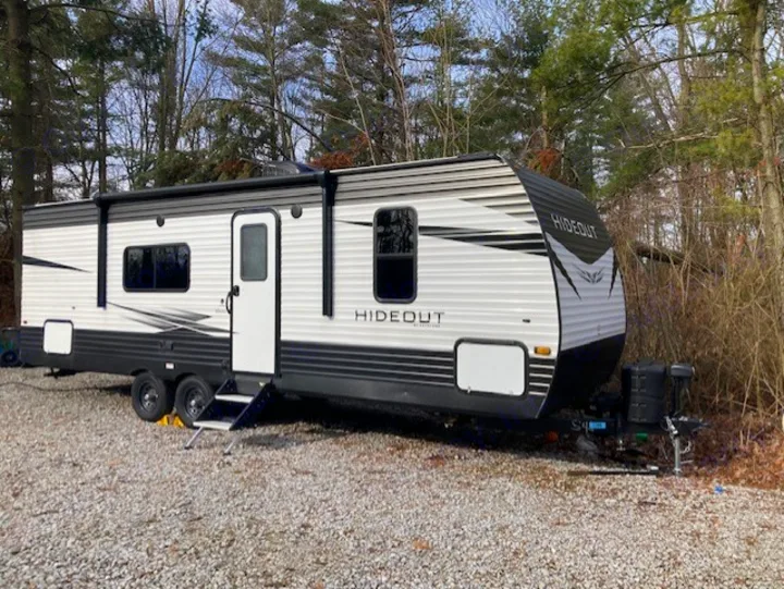 Modern 'Hideout' RV rental parked on gravel with extended steps, surrounded by trees.. Keystone RV Hideout 2021