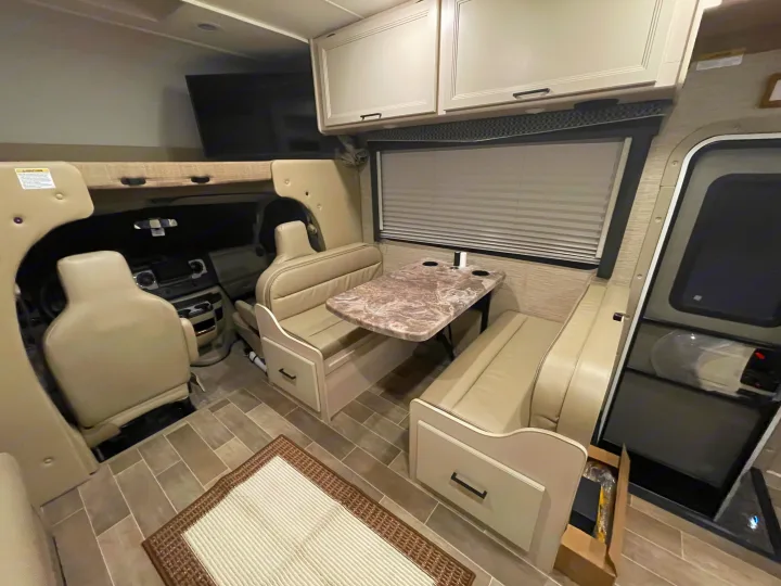Spacious RV rental interior with dinette, swivel seats, overhead bunk/TV, and storage for comfortable travel.. Thor Chateau 2022