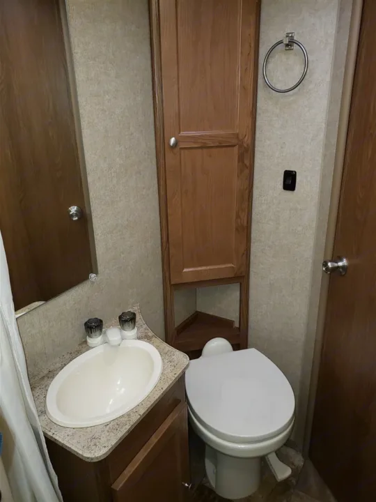Compact RV rental bathroom featuring a sink, toilet, tall cabinet, and mirror, designed for convenient travel.. Forest River Coachmen Leprechaun 2017