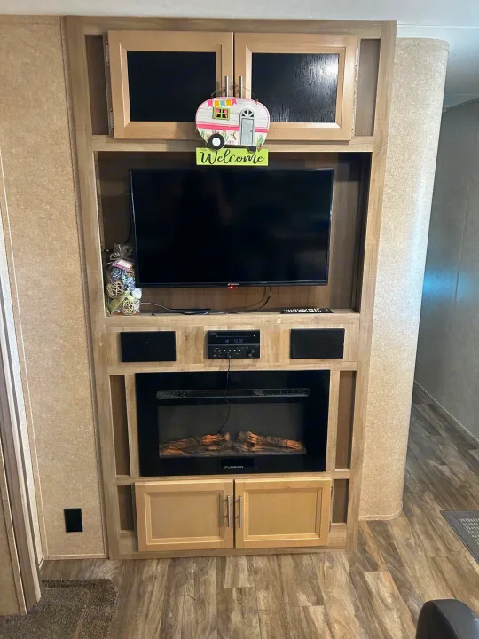Modern **RV rental** interior with entertainment unit, TV, electric fireplace, and light wood cabinetry for a cozy living space.. Coachmen Catalina 2019