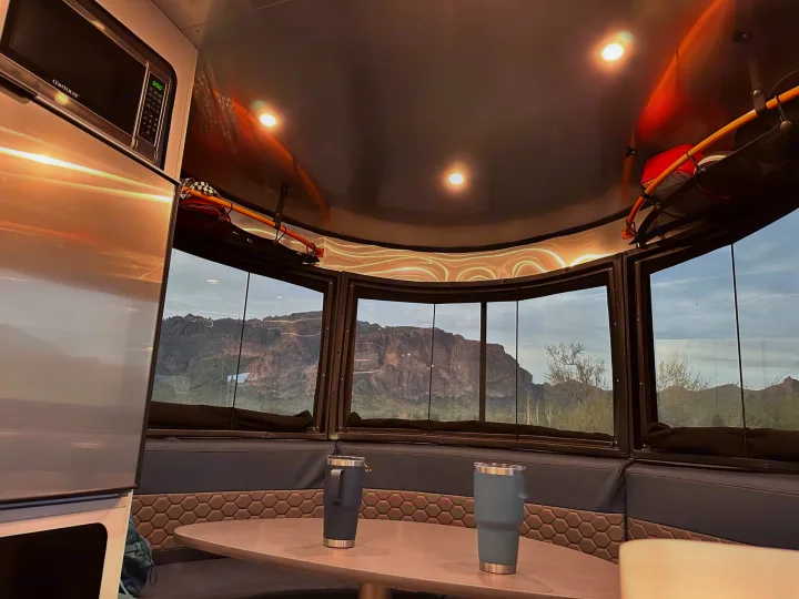 Inside a spacious RV rental, offering panoramic desert mountain views. Features comfy seating, table with tumblers, & microwave. Ideal for scenic travel.. Airstream Basecamp 2021