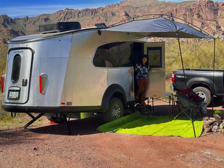 Woman exits an Airstream Basecamp RV rental in a desert mountain setting. Ideal for outdoor adventures and camping.. Airstream Basecamp 2021