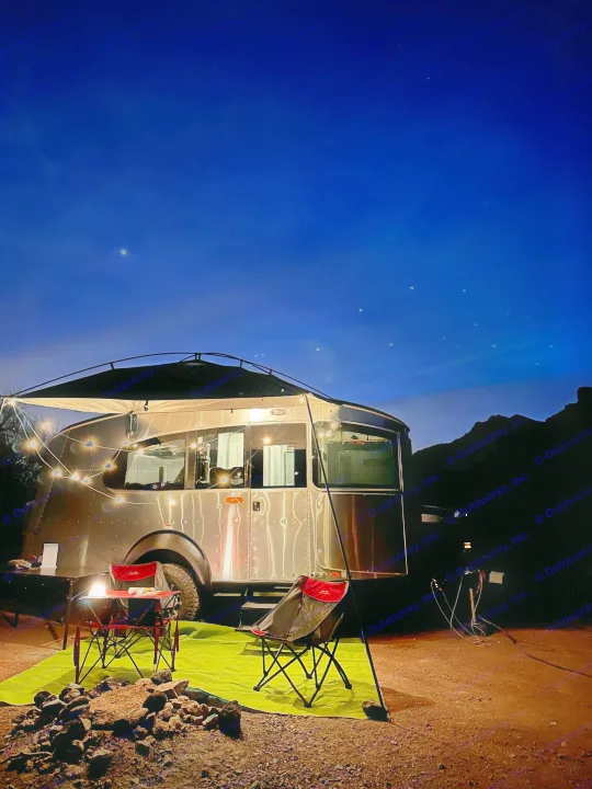 Peaceful night camping scene with an RV rental. An Airstream, string lights, and starry sky create a cozy outdoor living area.. Airstream Basecamp 2021