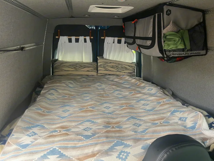 Cozy RV rental sleeping area features patterned bedding, pillows, and hanging storage.. Mercedes-Benz Sprinter 2021