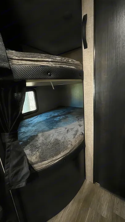 Inside an RV rental: two bunk beds with stylish grey bedding, a window with curtains, and modern cabinetry.. Jayco Jay Flight SLX 2022