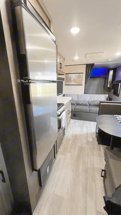 Inside an rv rental: a compact kitchen with a stainless fridge, a living area with a sofa and blanket, and a dining table. Wood-look floor.. Jayco Jay Flight SLX 2022