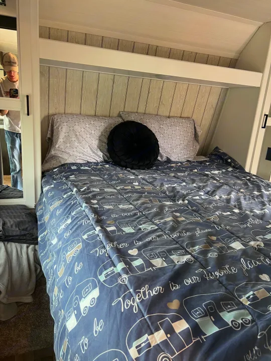 Inside a comfy RV rental, showing a bed with a fun camper-themed comforter.. Keystone Hideout 2022