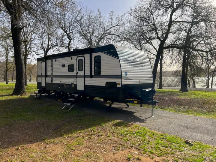RV rental travel trailer set up at a scenic lakeside campsite with bare trees. Ideal for a nature getaway.. Keystone Hideout 2022