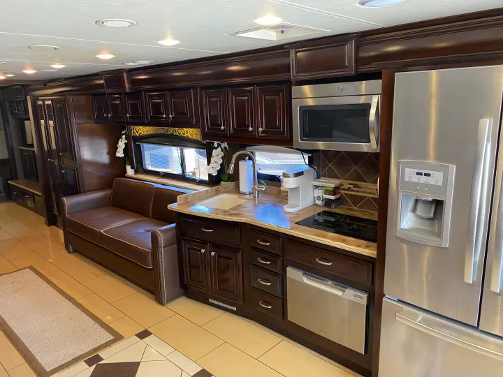 Luxurious RV rental interior: well-appointed kitchen with stainless appliances, dark cabinets, and comfortable leather sofa.. Thor Motor Coach Tuscany 2015