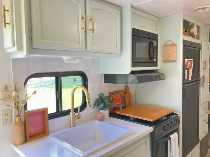 Cozy & bright RV rental kitchen featuring light green cabinets, gold fixtures, a sink, microwave, and stove.. Forest River Other 2013