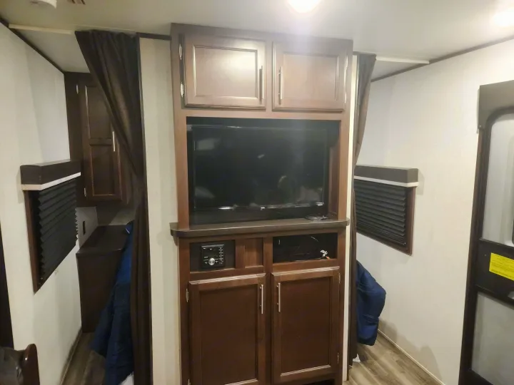 Inside an RV rental: a compact living area featuring an entertainment unit with TV, stereo, and ample storage cabinets.. Jayco Jay Flight SLX 2019