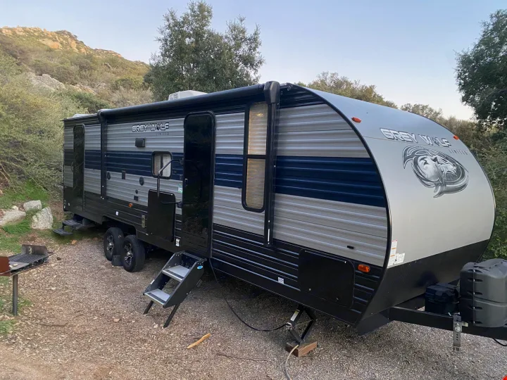 Grey Wolf RV rental travel trailer at a gravel campsite, with mountains and trees in the background, ready for outdoor adventure.. Forest River Cherokee Grey Wolf 2021