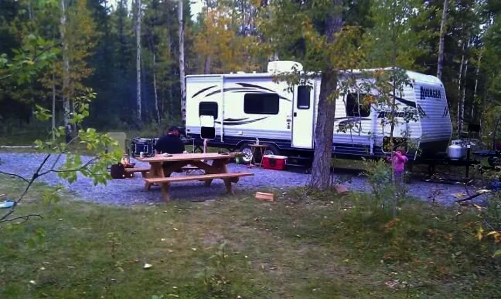 Enjoying an RV rental at a serene forest campsite, with a white travel trailer, man at picnic table, and child.. Avenger LT 2012