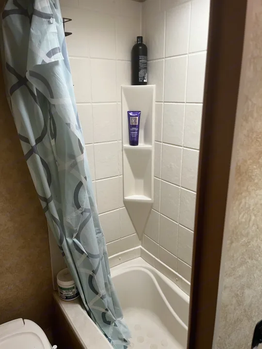 RV rental bathroom features: compact shower/tub, patterned curtain, and shelves with shampoo/conditioner bottles.. Avenger LT 2012