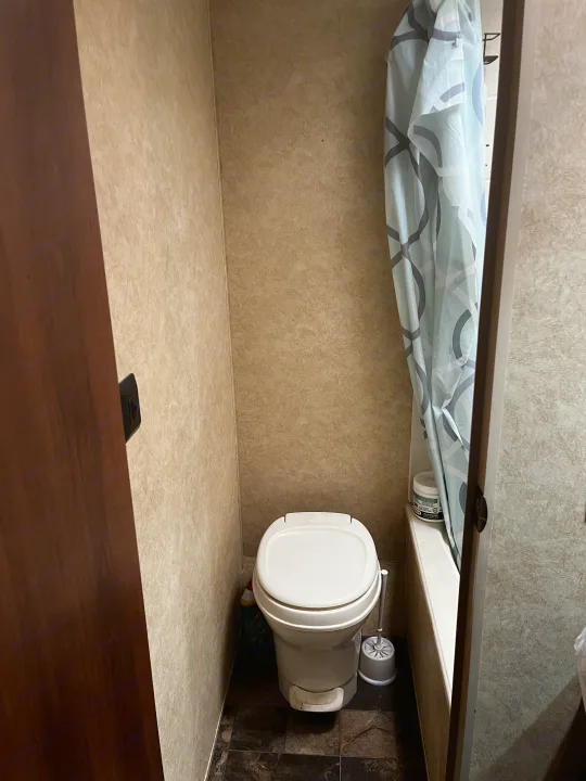RV rental bathroom with a compact white toilet, light blue shower curtain, and small tub, seen from the doorway.. Avenger LT 2012