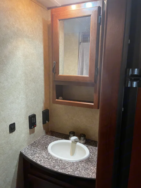 This RV rental features a compact bathroom with a vanity, sink, and mirrored medicine cabinet reflecting a shower.. Avenger LT 2012