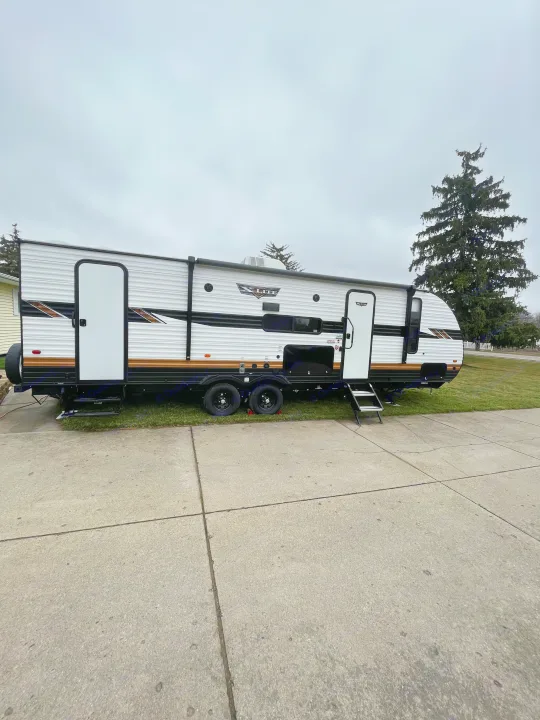 Experience travel with this X-Lite RV rental, a white travel trailer parked on a concrete driveway under an overcast sky.. Wildwood X-Lite BH 263 2023