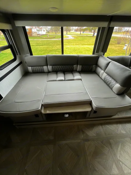Comfortable RV rental living space: a large gray convertible sofa/bed by windows overlooking a green lawn.. Wildwood X-Lite BH 263 2023