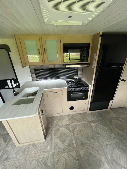 RV rental kitchen: modern light wood cabinets, double sink, gas stove, microwave, and fridge.. Wildwood X-Lite BH 263 2023