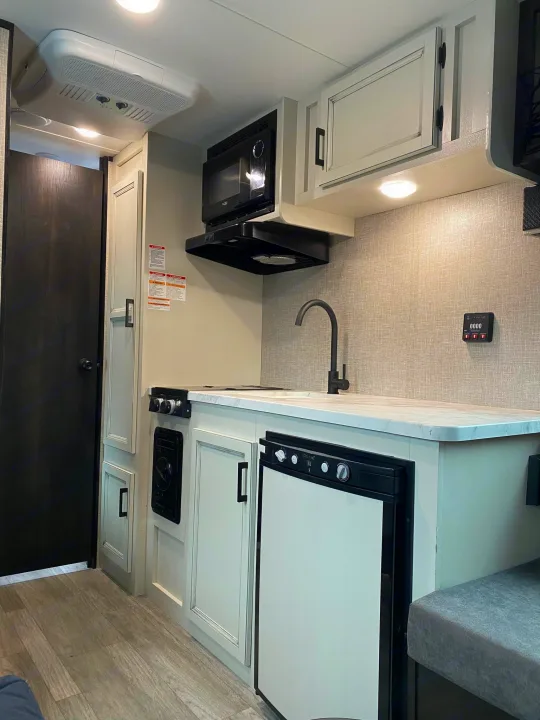 RV rental interior: functional kitchen with sink, stove, microwave, fridge, and control panel. Compact for travel.. Jayco Jay Flight SLX 2022