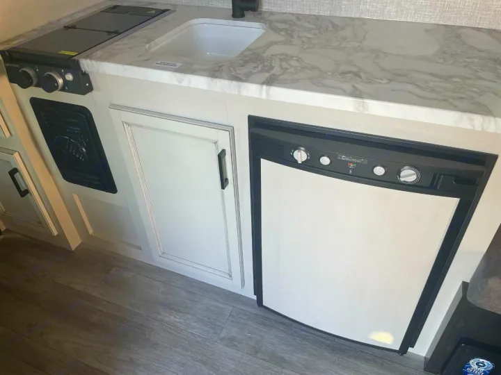Cozy RV rental kitchen featuring a marble-look counter, sink, Greystone stove, and Dometic refrigerator with storage cabinets.. Jayco Jay Flight SLX 2022