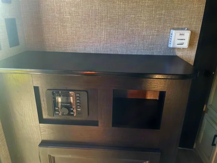 RV rental interior showing an iRV Technologies stereo, a Dometic thermostat, and storage cubby on a dark cabinet.. Jayco Jay Flight SLX 2022