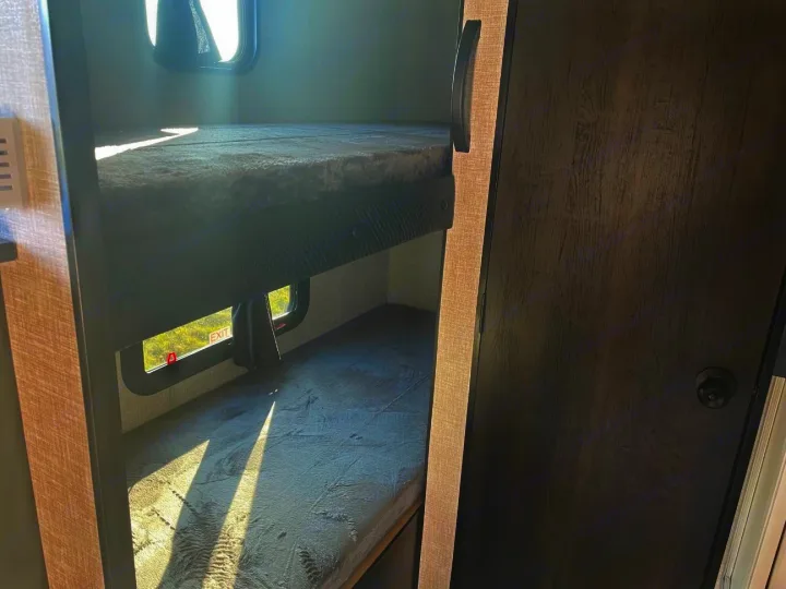 Inside an RV rental: two sunlit bunk beds. The lower bunk features an emergency exit window, ideal for family adventures.. Jayco Jay Flight SLX 2022
